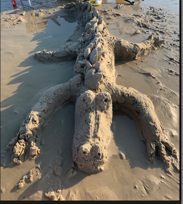 Large crocodile sculpture shaped from beach sand