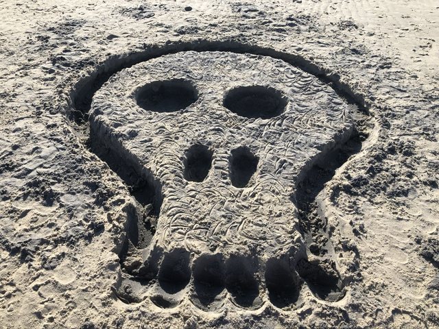 Large skull relief sculpted in beach sand
